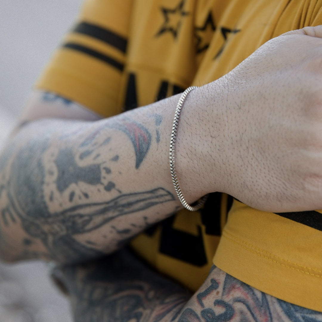 Άντρας με τατουάζ που φορά το Box Silver Bracelet 2mm από ανοξείδωτο ατσάλι σε ασημί χρώμα.